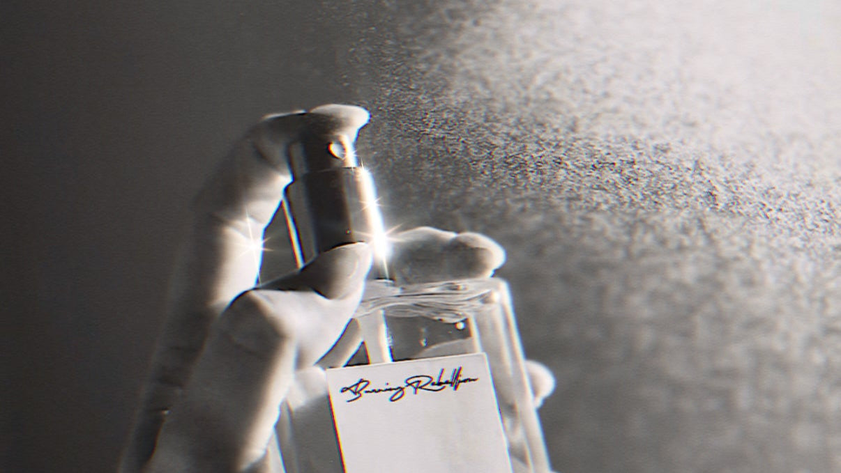 Hand holding a clear perfume bottle with a dark background