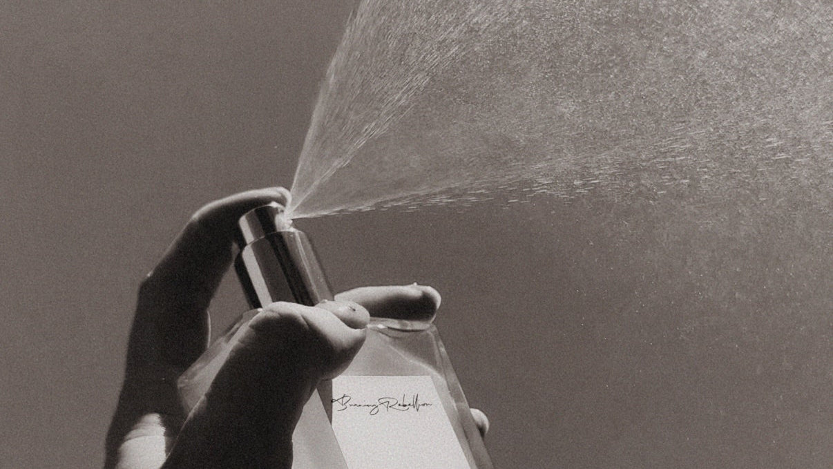 Hand holding a spray bottle with a label, against a plain background